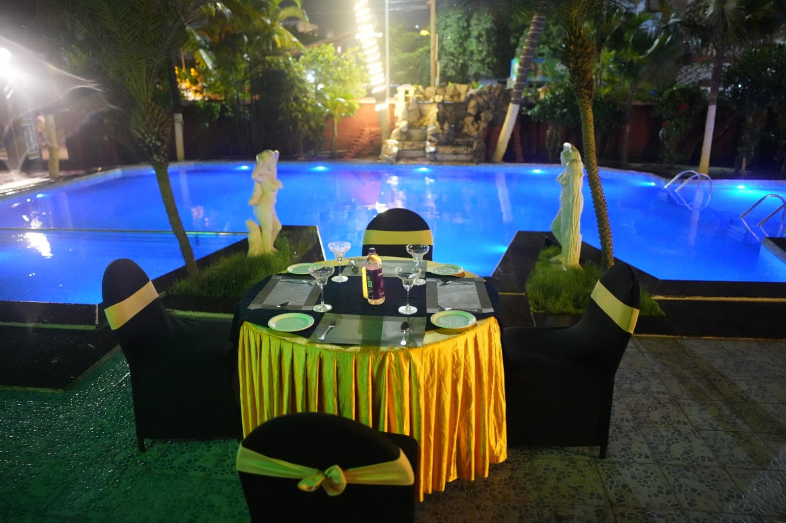 Night poolside dinner table with blue-lit pool
